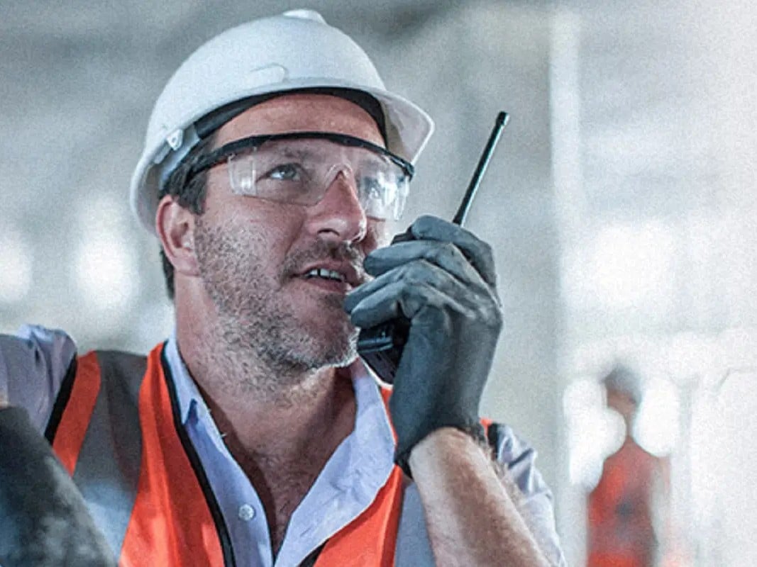 Operario de una refinería con casco y chaleco hablando por radio Hytera